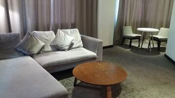 A modern hotel room with a grey sofa, a round wooden coffee table, and a small round table with two chairs.