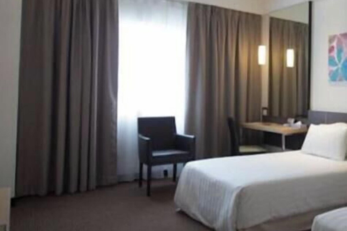 Une chambre d’hôtel avec un lit, une chaise, un bureau et une grande fenêtre avec des rideaux.