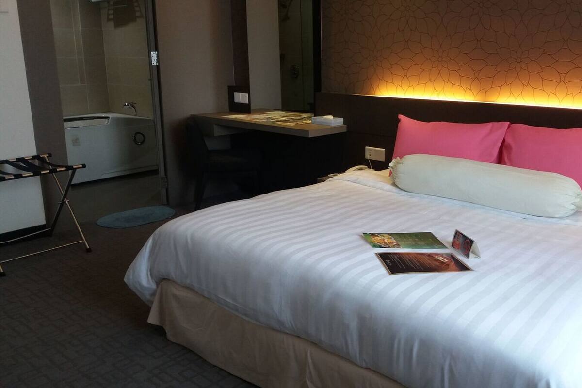 A hotel room with a large bed, a bedside table, a mirror, and a desk with a chair.