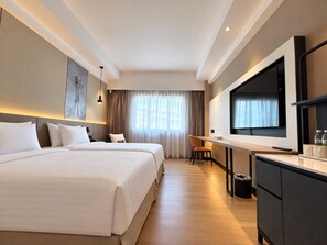 A hotel room with two beds, a desk, a TV, and a large window with curtains.