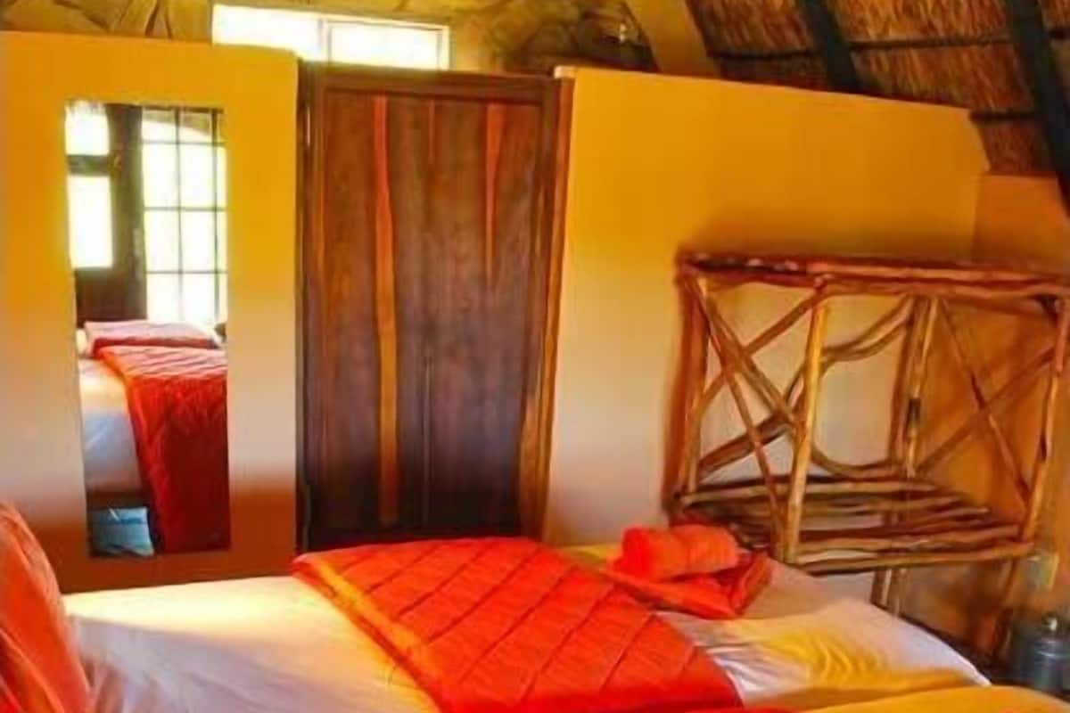 A room with two beds, wooden furniture, and a thatched roof.