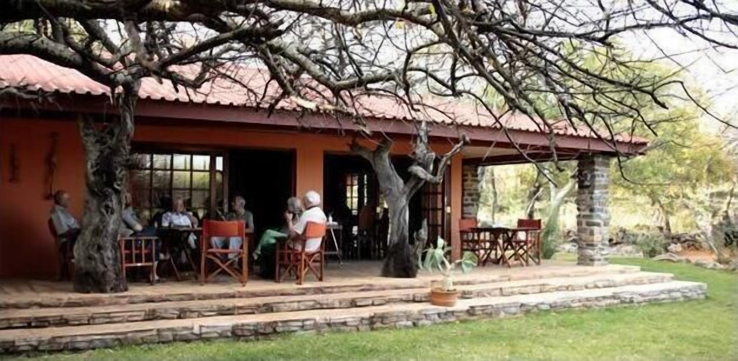 A rustic building with a red roof, outdoor seating, and a large tree in the foreground.