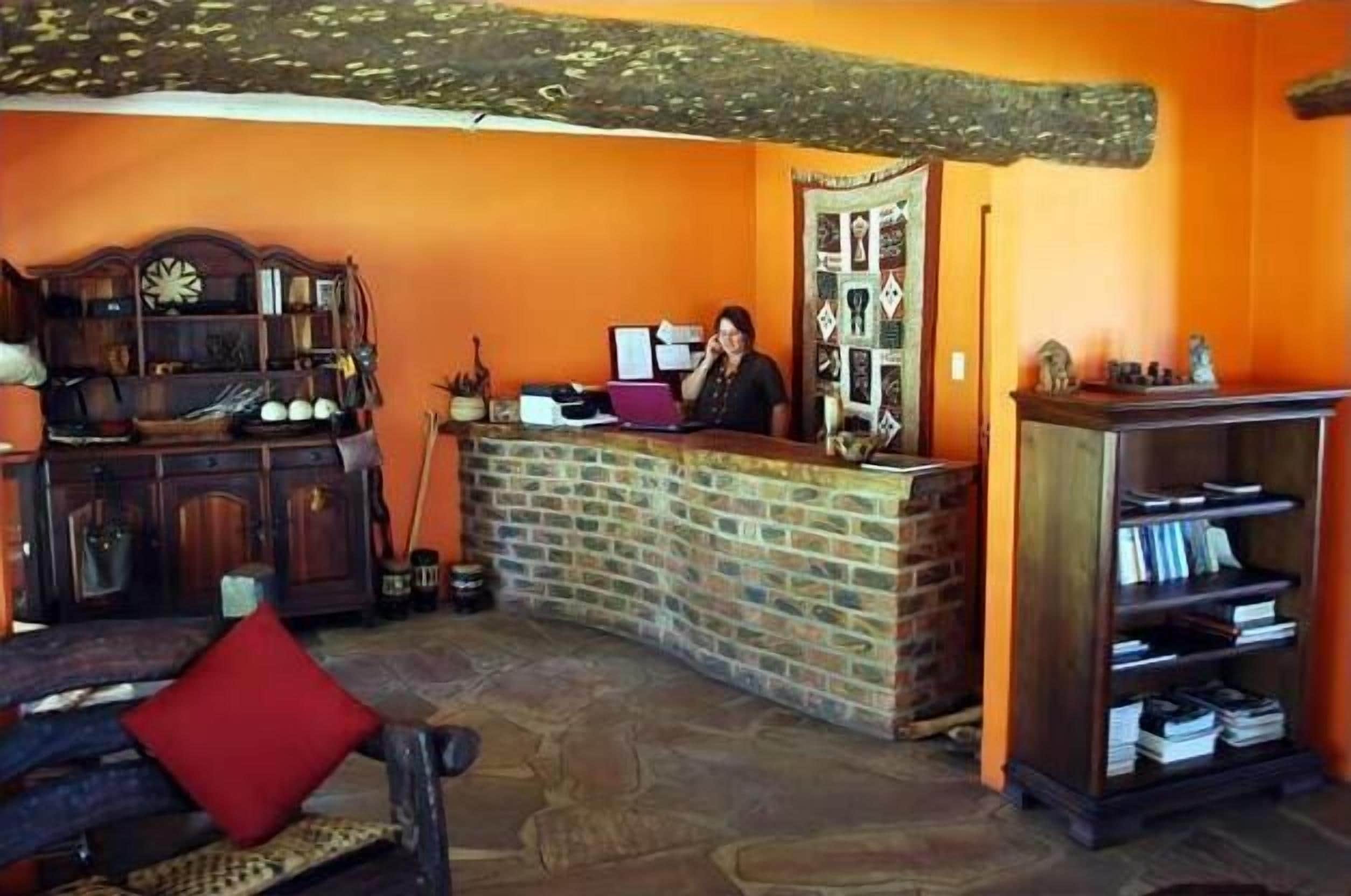 Un espace d’accueil avec un bureau en bois, un ordinateur portable et une personne debout derrière.