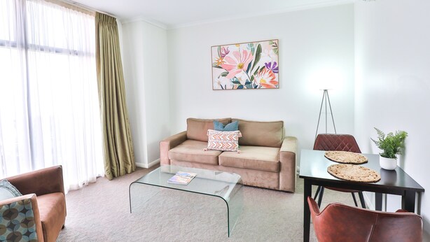 Un salon avec un canapé, une table basse et des fauteuils. Il y a un tableau au mur et une plante sur une table.