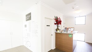 Ein Empfangsbereich mit einem Holztresen, einer Vase mit roten Blumen und Informationsplakaten an der Wand.