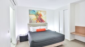 Ein modernes Schlafzimmer mit einem großen Bett, einem Nachttisch, einer Stehlampe und einem farbenfrohen abstrakten Gemälde an der Wand.