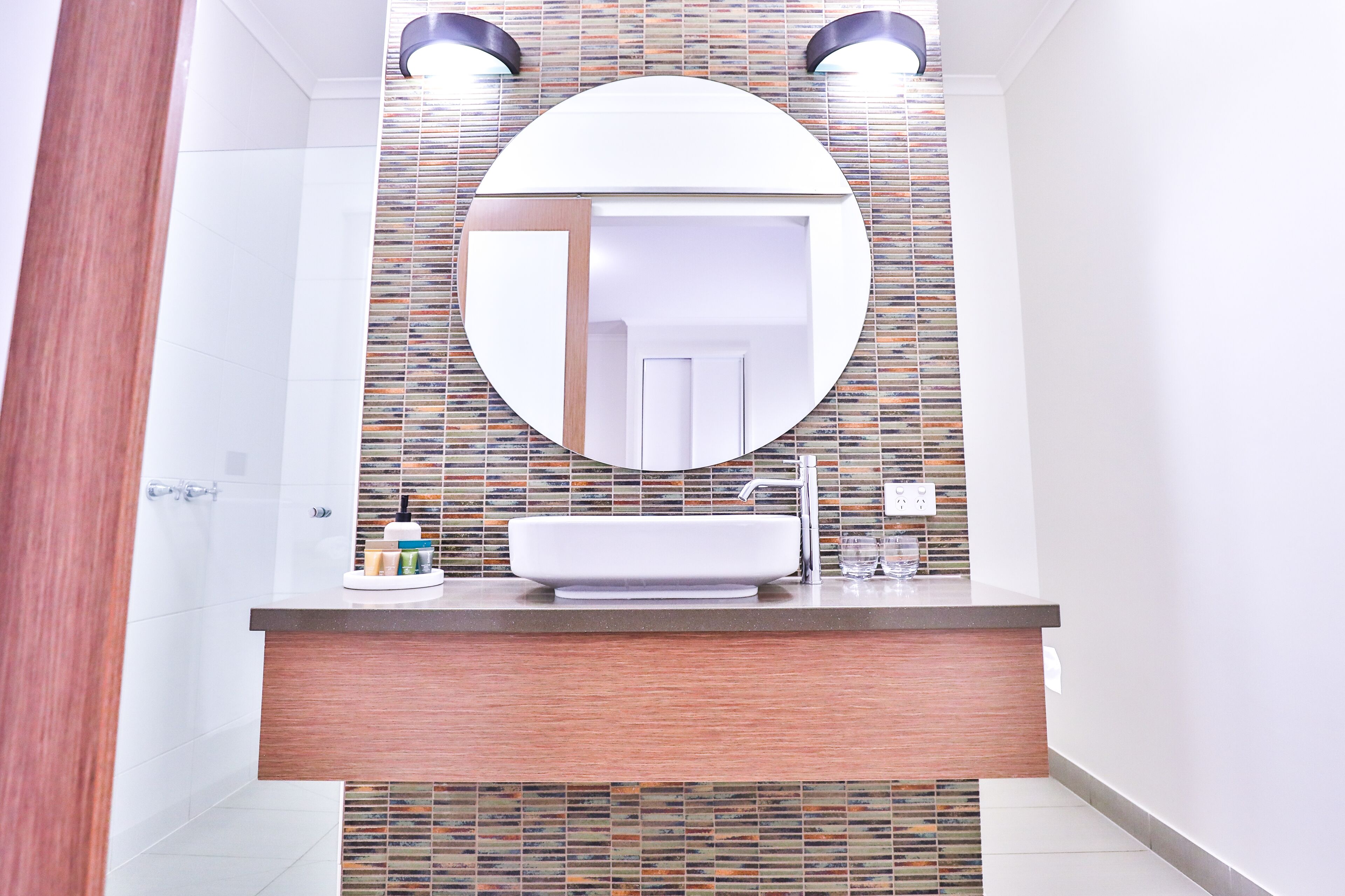 A bathroom with a round mirror, a rectangular sink, and a tiled backsplash.