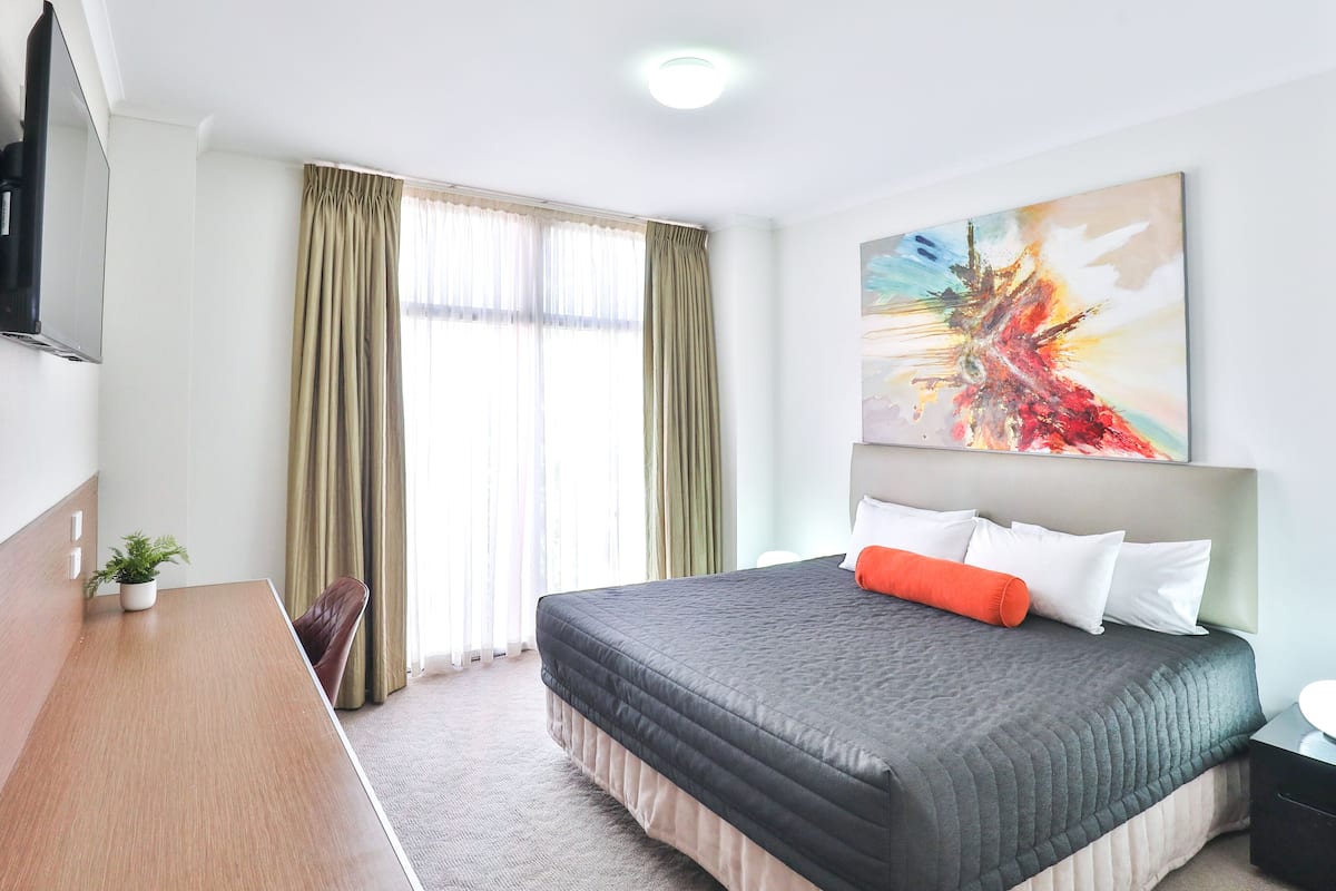 Une chambre d’hôtel avec un lit, un bureau, une chaise, une télévision et un tableau au mur.