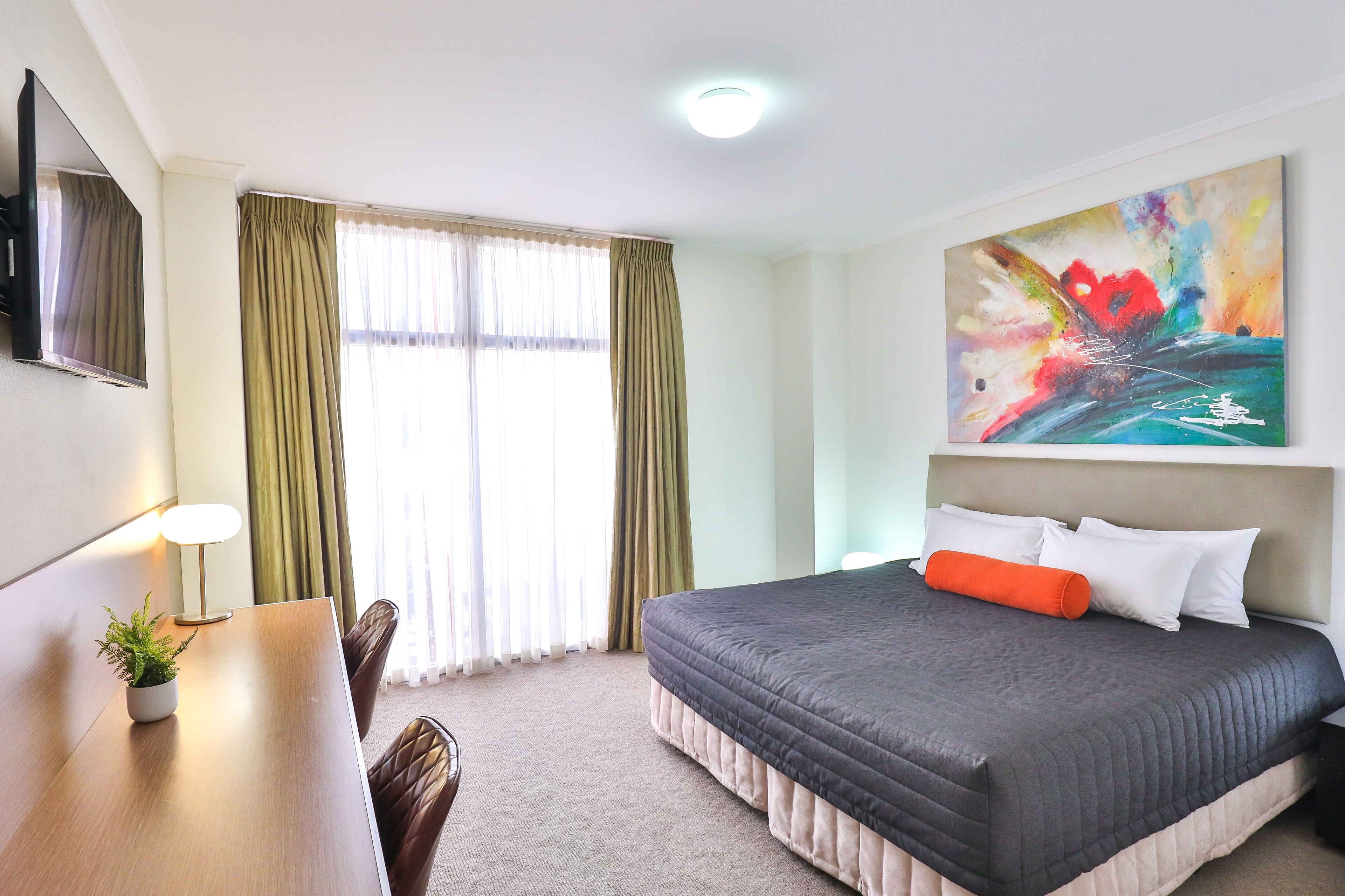 Ein Hotelzimmer mit Bett, Schreibtisch, Stuhl, Fernseher und einem Bild an der Wand.