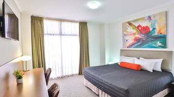 Ein Hotelzimmer mit Bett, Schreibtisch, Stuhl, Fernseher und einem Bild an der Wand.