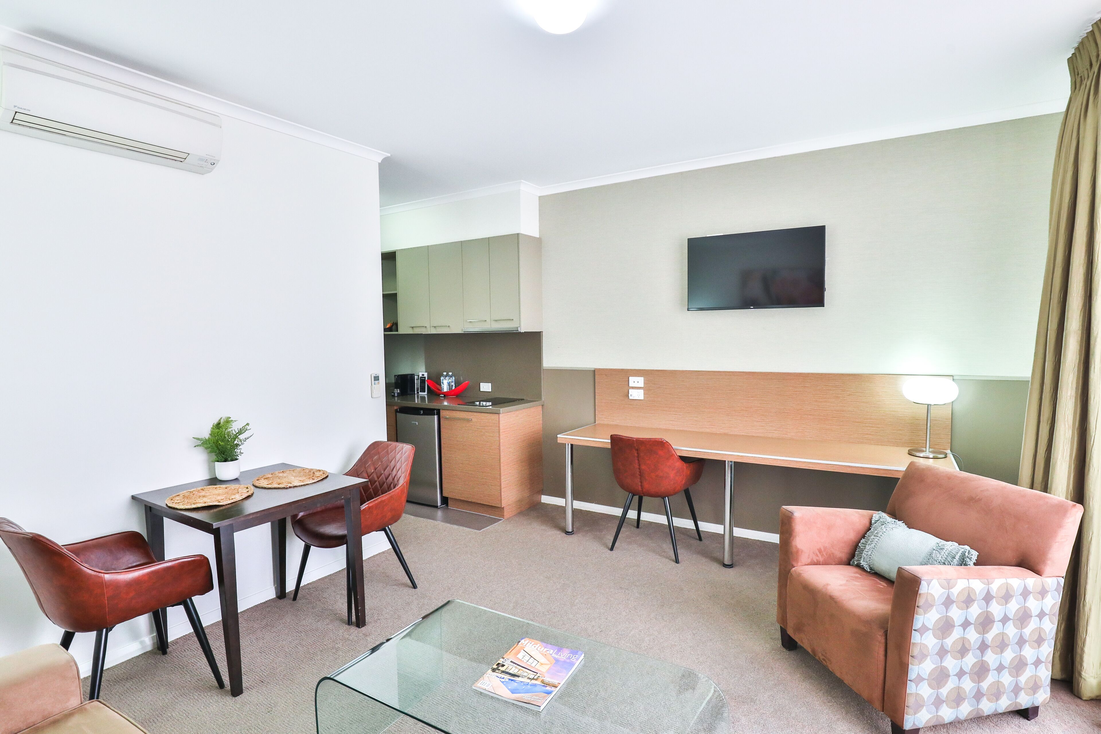 A compact living space with a kitchenette, a dining area with a table and chairs, a sofa, and a TV mounted on the wall.