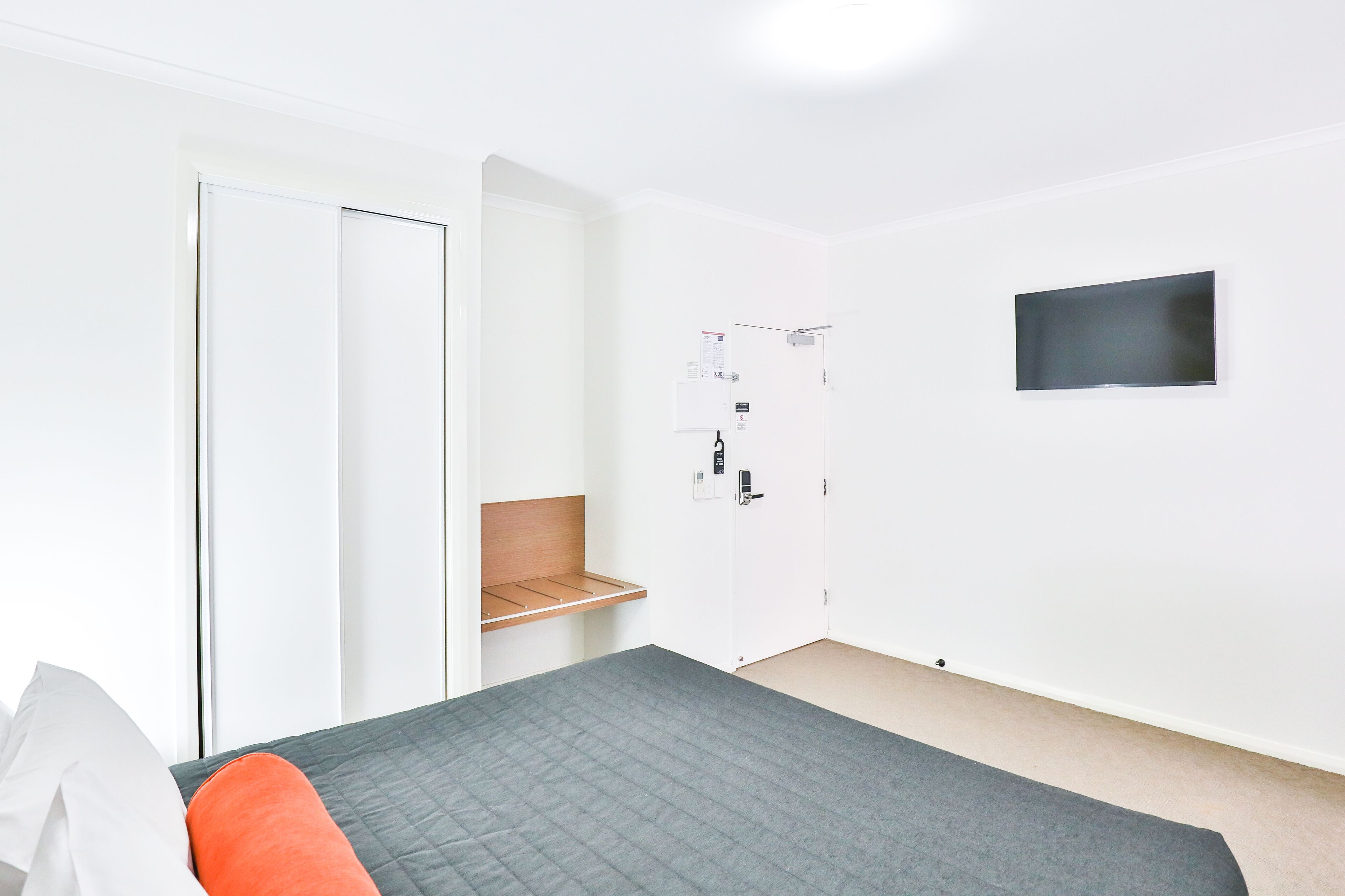 Ein Schlafzimmer mit Bett, Wandfernseher, Kleiderschrank und einer Tür mit Korkwand.