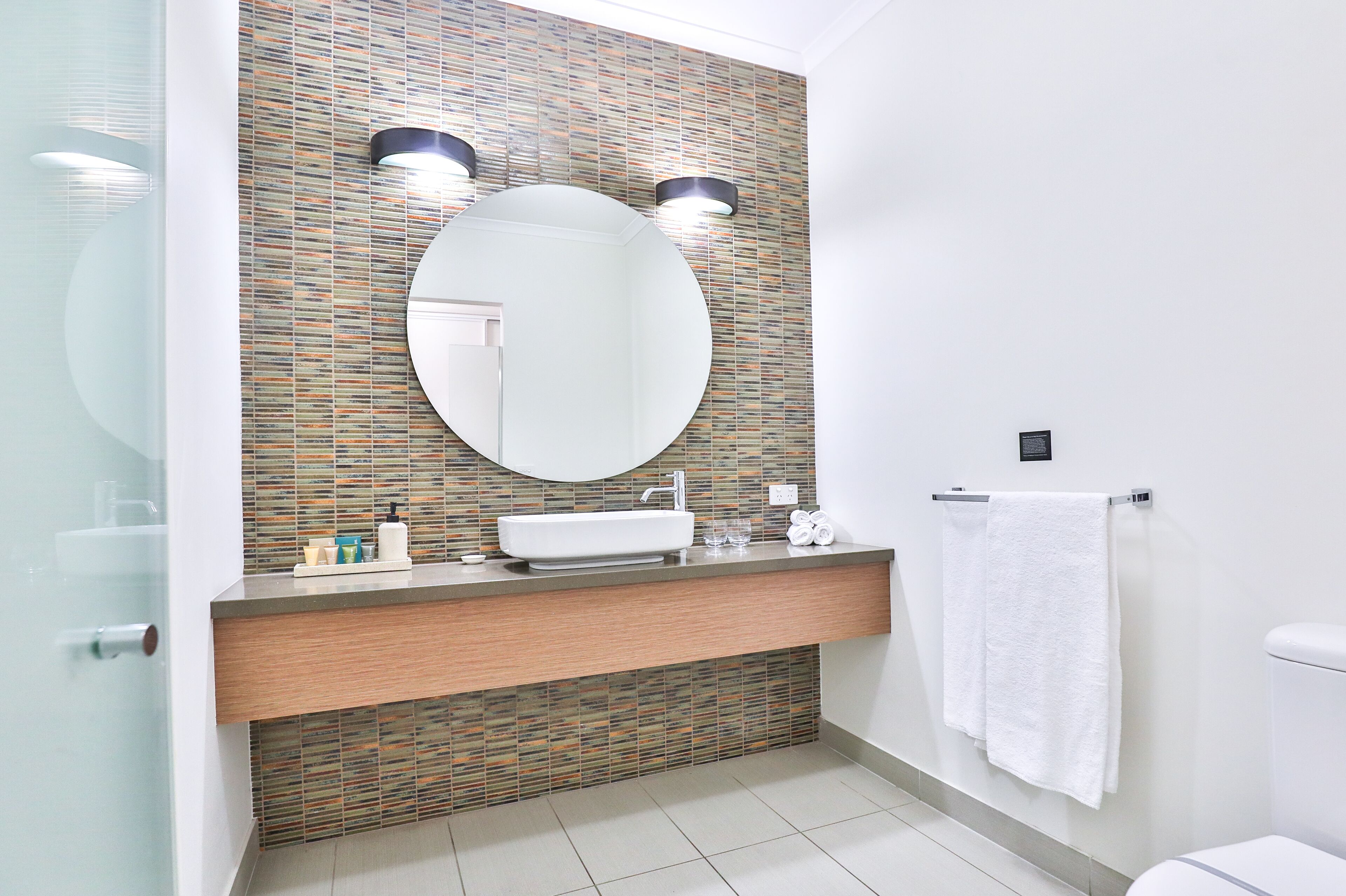 A modern bathroom with a large mirror, two wall-mounted lights, a sink, and a toilet.