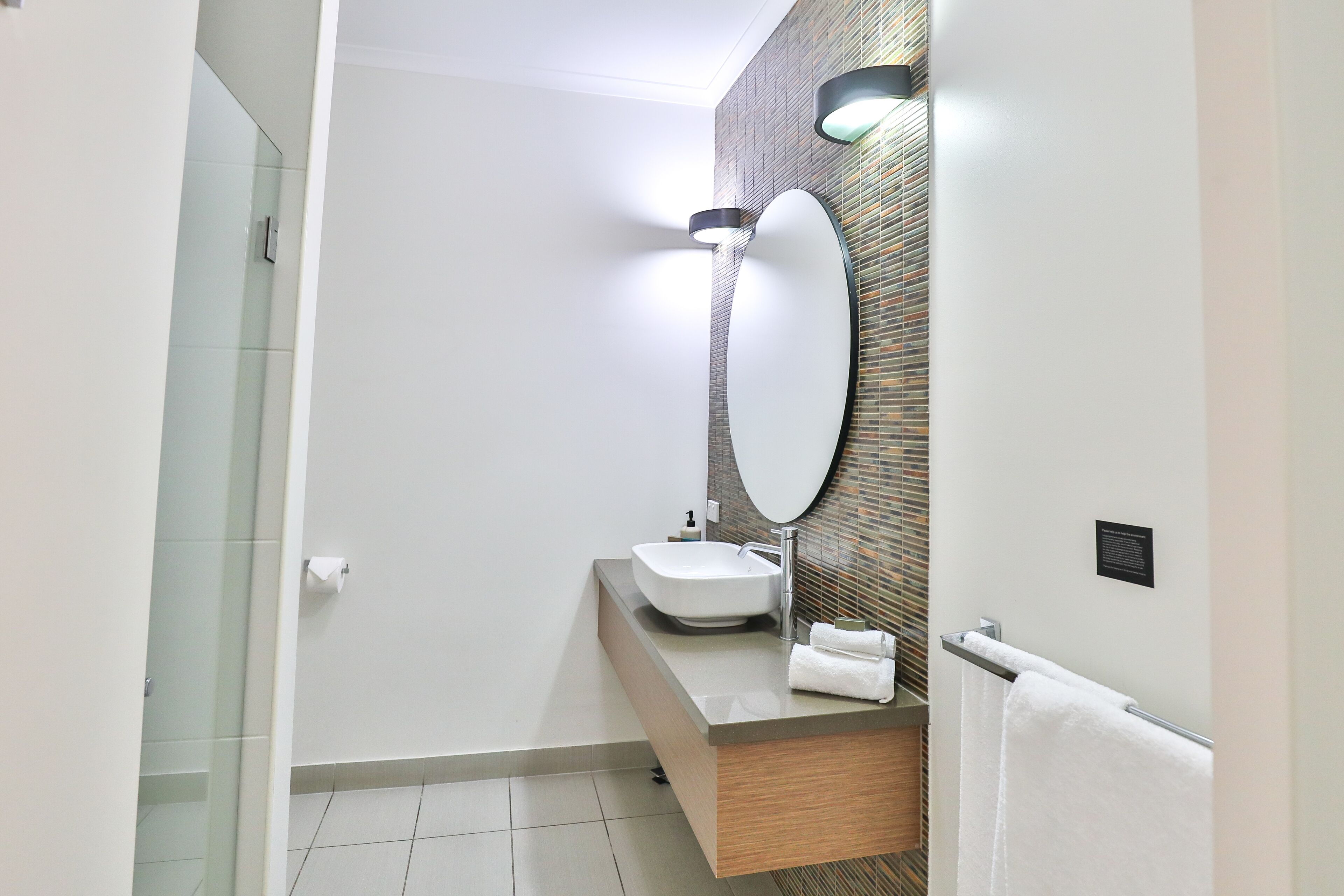 A modern bathroom with a white sink, a large mirror, and a towel rack.