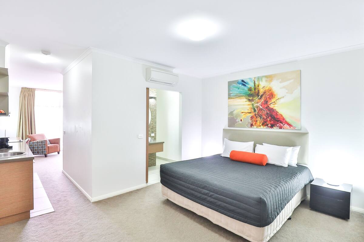 Une chambre d’hôtel moderne avec un grand lit, un tableau au mur et une vue sur la ville par la fenêtre.