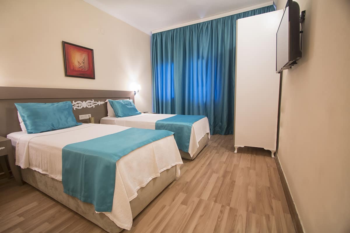 Quarto de hotel com duas camas, televisão e uma janela grande com cortinas.