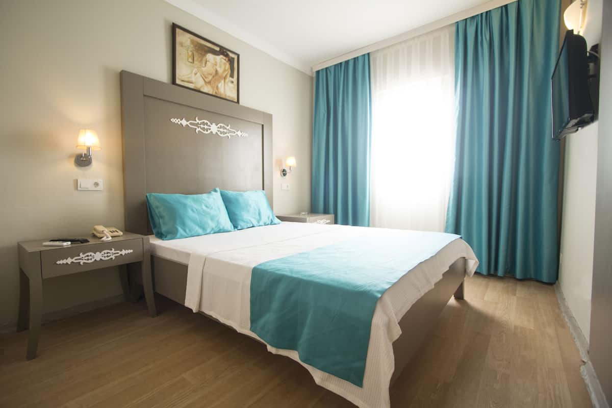 Quarto de hotel bem organizado com cama, mesas de cabeceira, luminária na parede e um quadro.