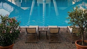 Zona junto a la piscina con una estructura de piedra, banderas y sillones de descanso.