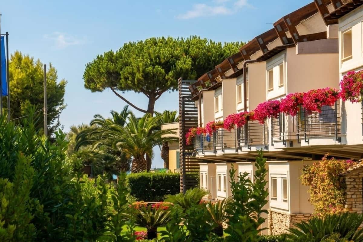 A building with balconies adorned with flowers, a flag, and lush greenery.