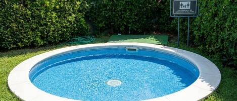 A circular swimming pool with a tiled edge, surrounded by grass and a hedge.