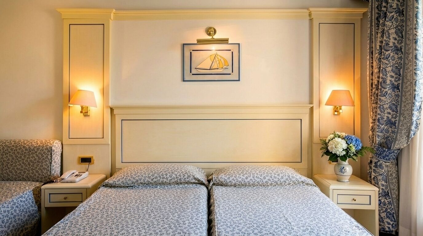A hotel room with two beds, a headboard, wall-mounted lamps, a framed picture, a telephone, and a floral arrangement.