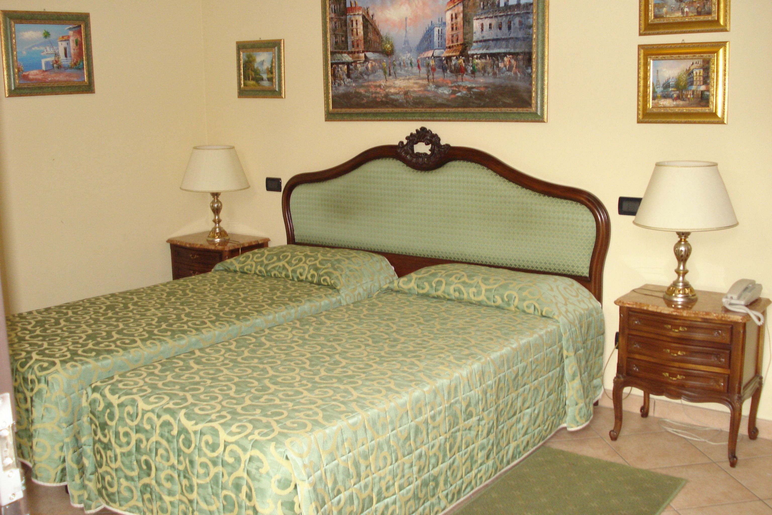 Una cama doble con una colcha verde estampada, dos mesitas de noche con lámparas, y un cuadro en la pared.