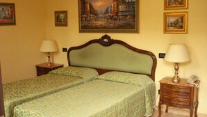 Habitación de hotel con dos camas, cabecero de madera, dos mesitas de noche con lámparas y un cuadro en la pared.