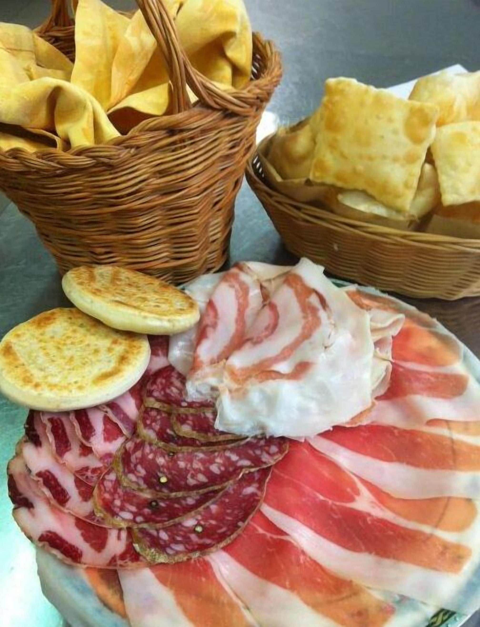 A plate of cured meats, including salami and prosciutto, accompanied by crackers and a basket of bread.
