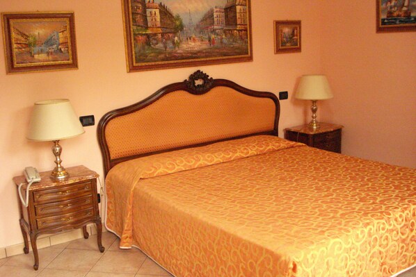 Une chambre avec un grand lit, deux tables de chevet avec des lampes et trois œuvres d’art encadrées accrochées au mur.