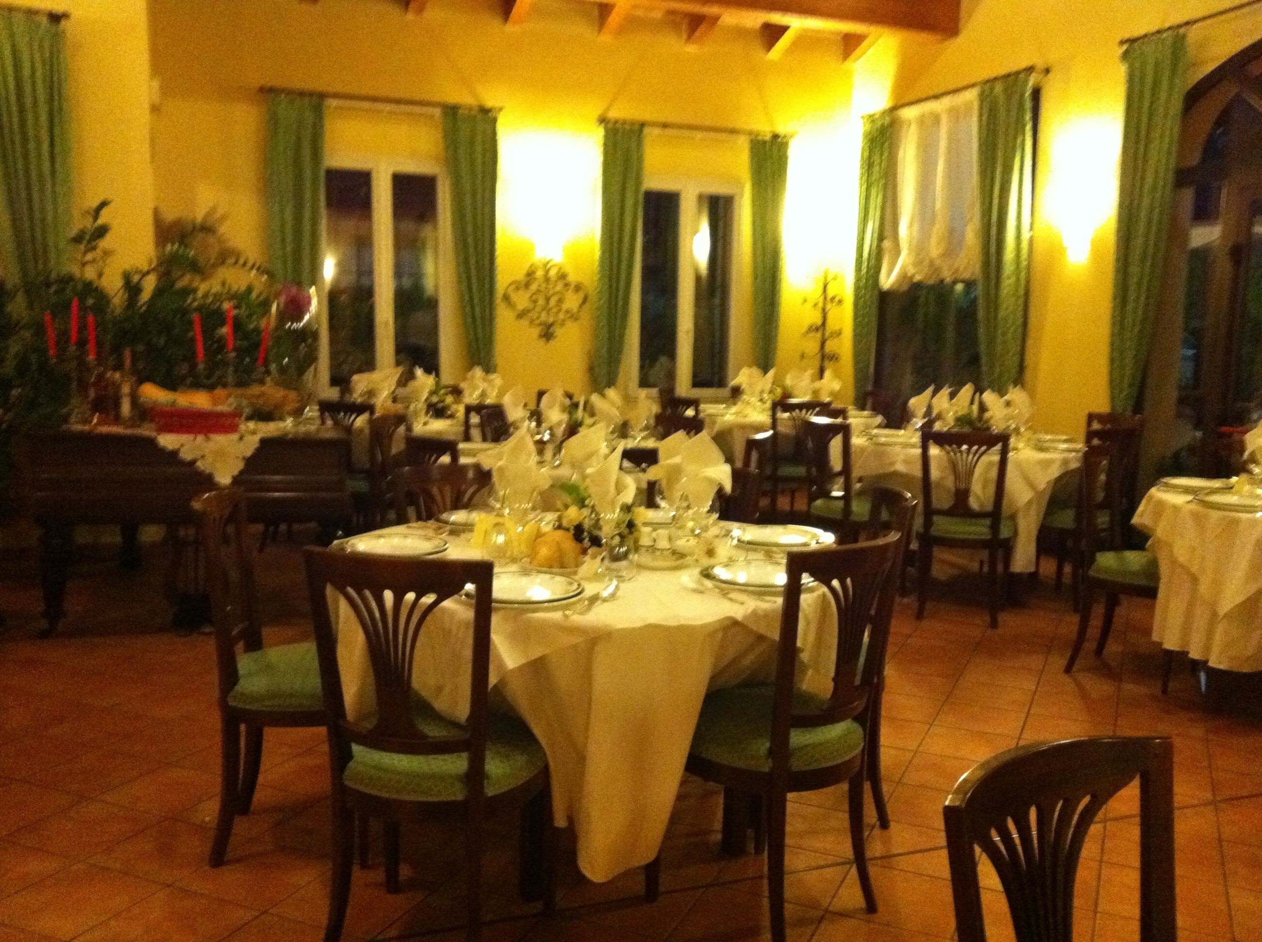 A restaurant with multiple tables set for dining, featuring green chairs and white tablecloths.