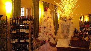 Una habitación con un árbol de Navidad blanco adornado con adornos, una estantería para vinos con botellas y una araña.