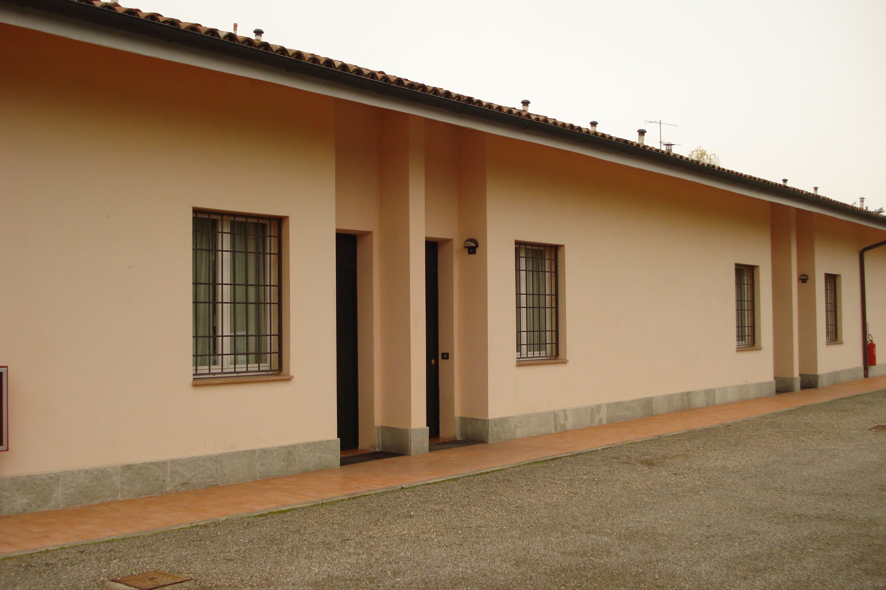 Un edificio con diverse finestre e porte, un tetto in tegole e un terreno sterrato.