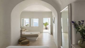 Une chambre avec une grande porte cintrée donnant sur un balcon, un lit avec une tête de lit blanche, une table de chevet et un miroir.