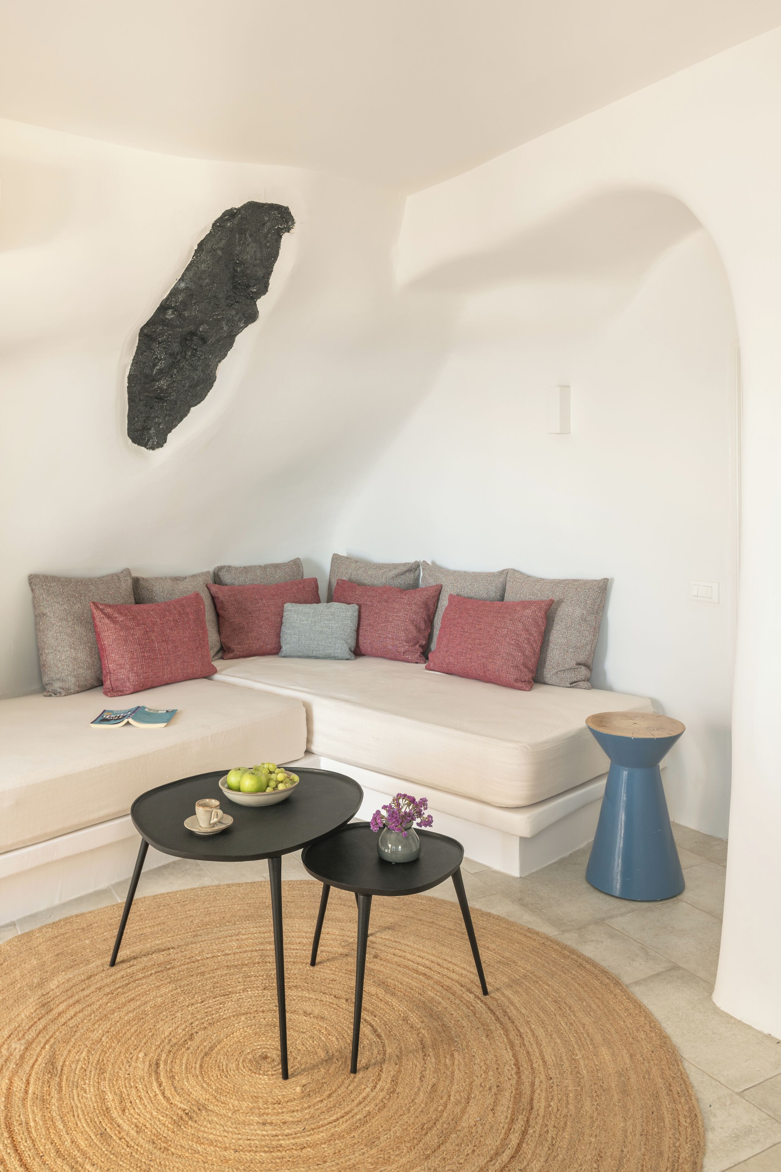 A modern living room with a sofa, two black tables, a woven rug, and a blue side table.