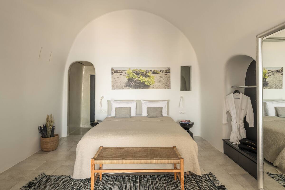 A bedroom with a large bed, a bench, a potted plant, and a painting on the wall.