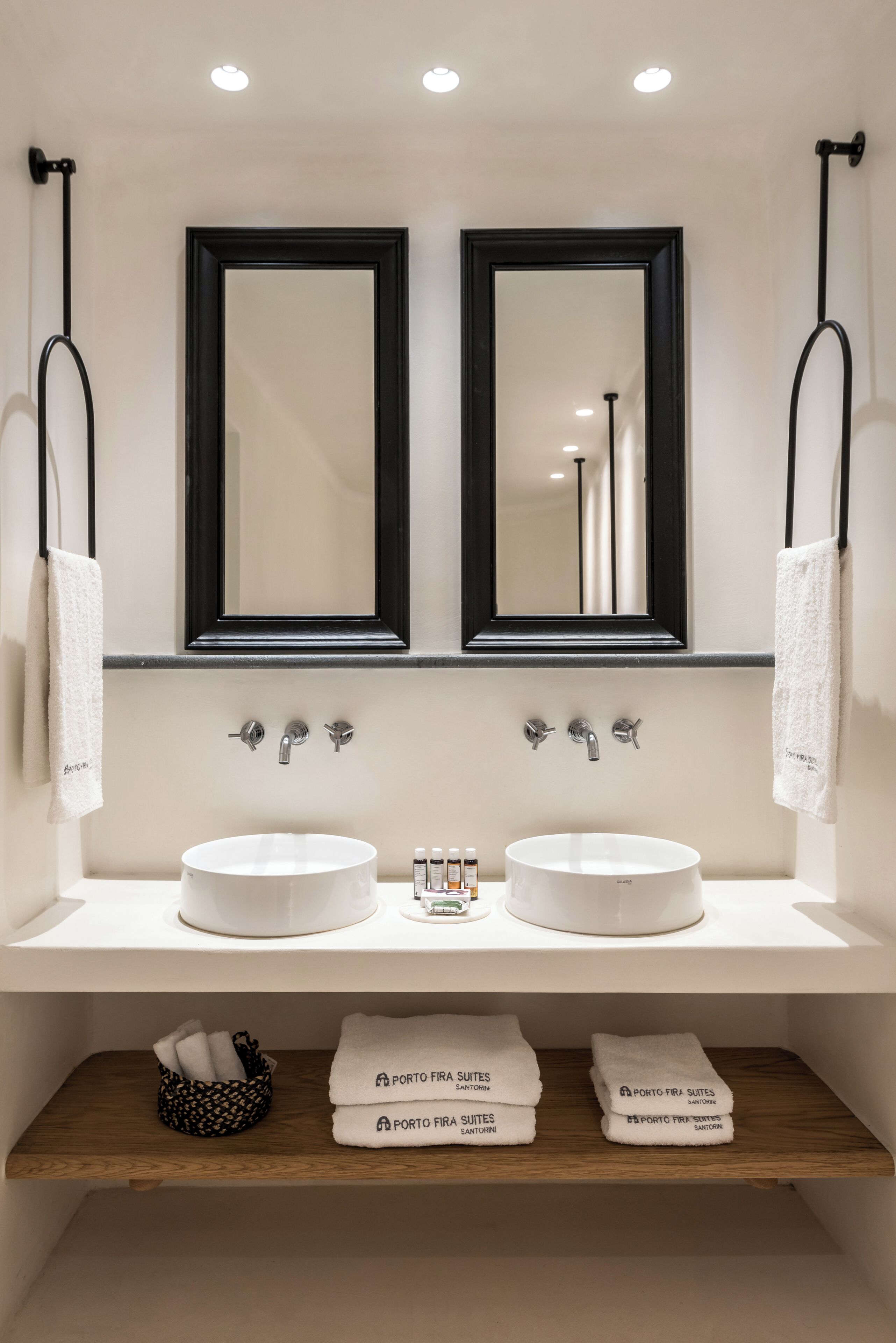 A modern bathroom with two sinks, a mirror, and a shelf with towels.