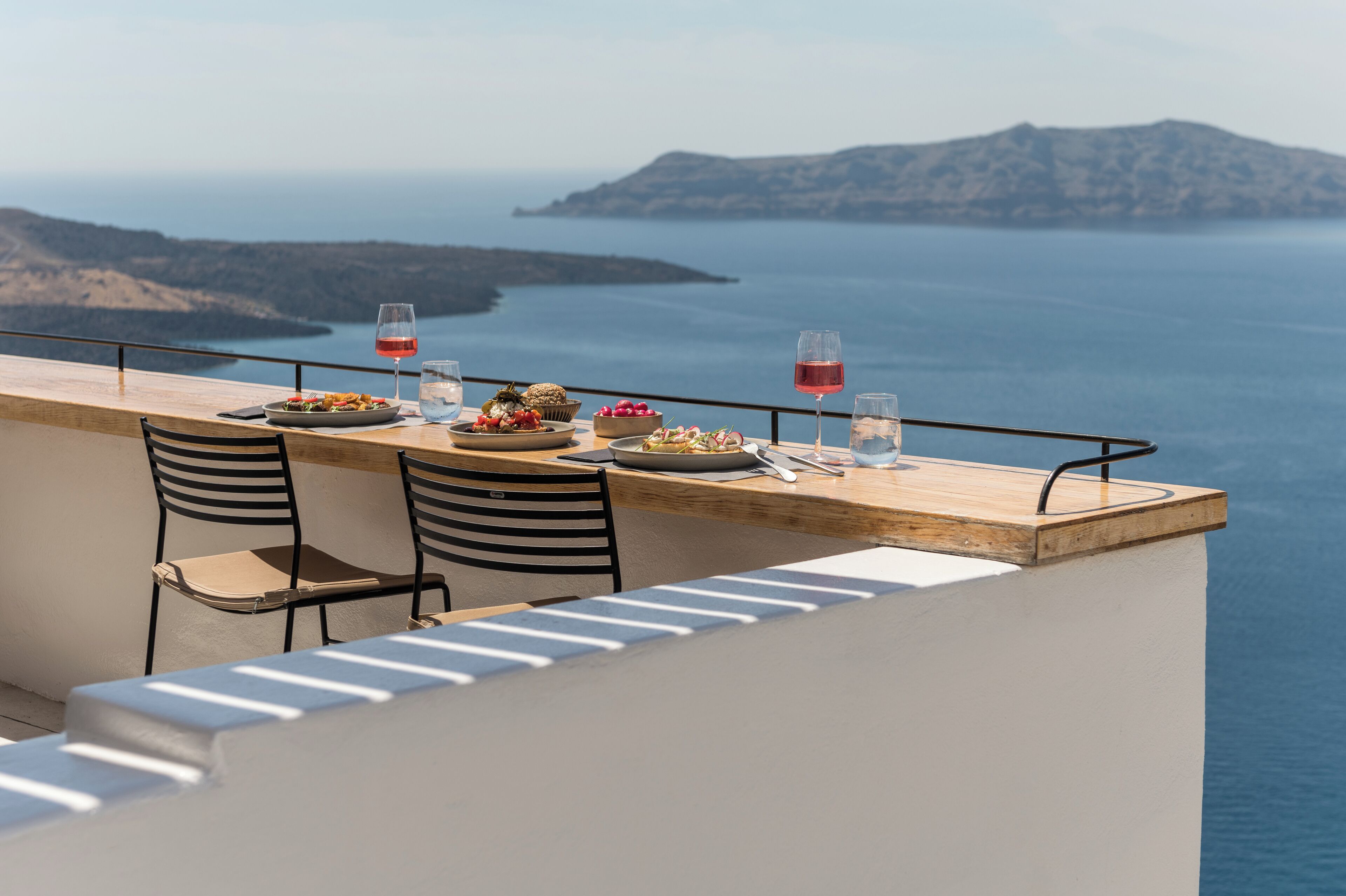 A terrace with a wooden table set for two, overlooking a coastal landscape.