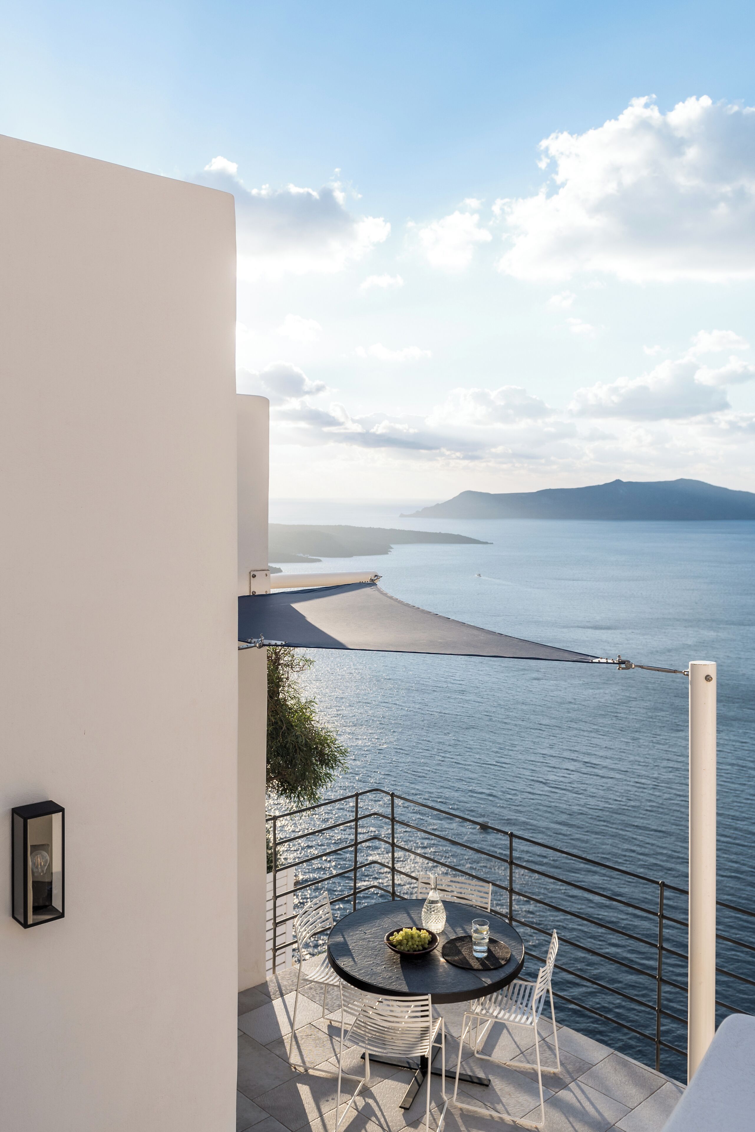 Un balcon avec une table et des chaises donnant sur une étendue d’eau et sur une terre lointaine.