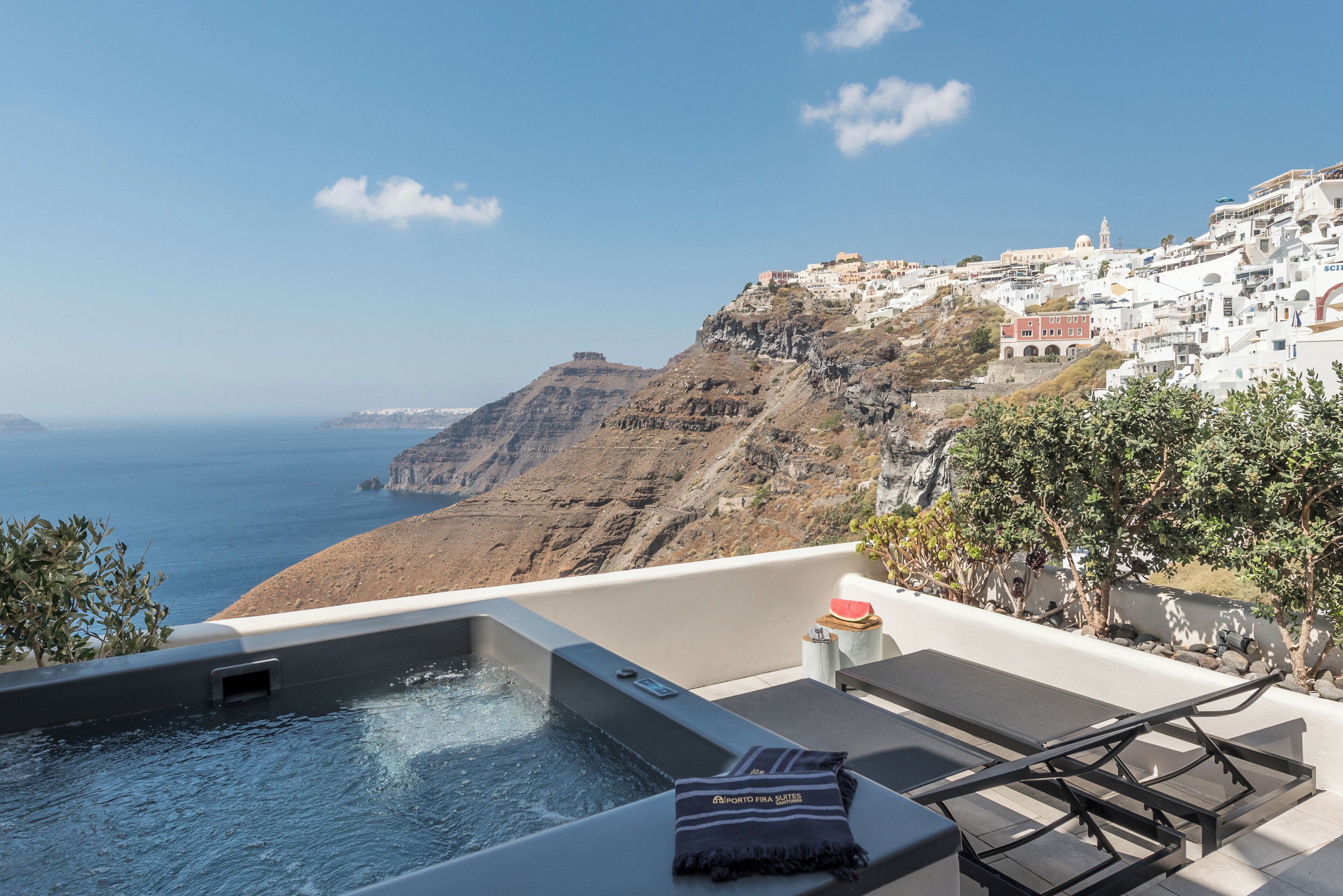A rooftop terrace with a hot tub, lounge chairs, and a view of the sea and coastal buildings.