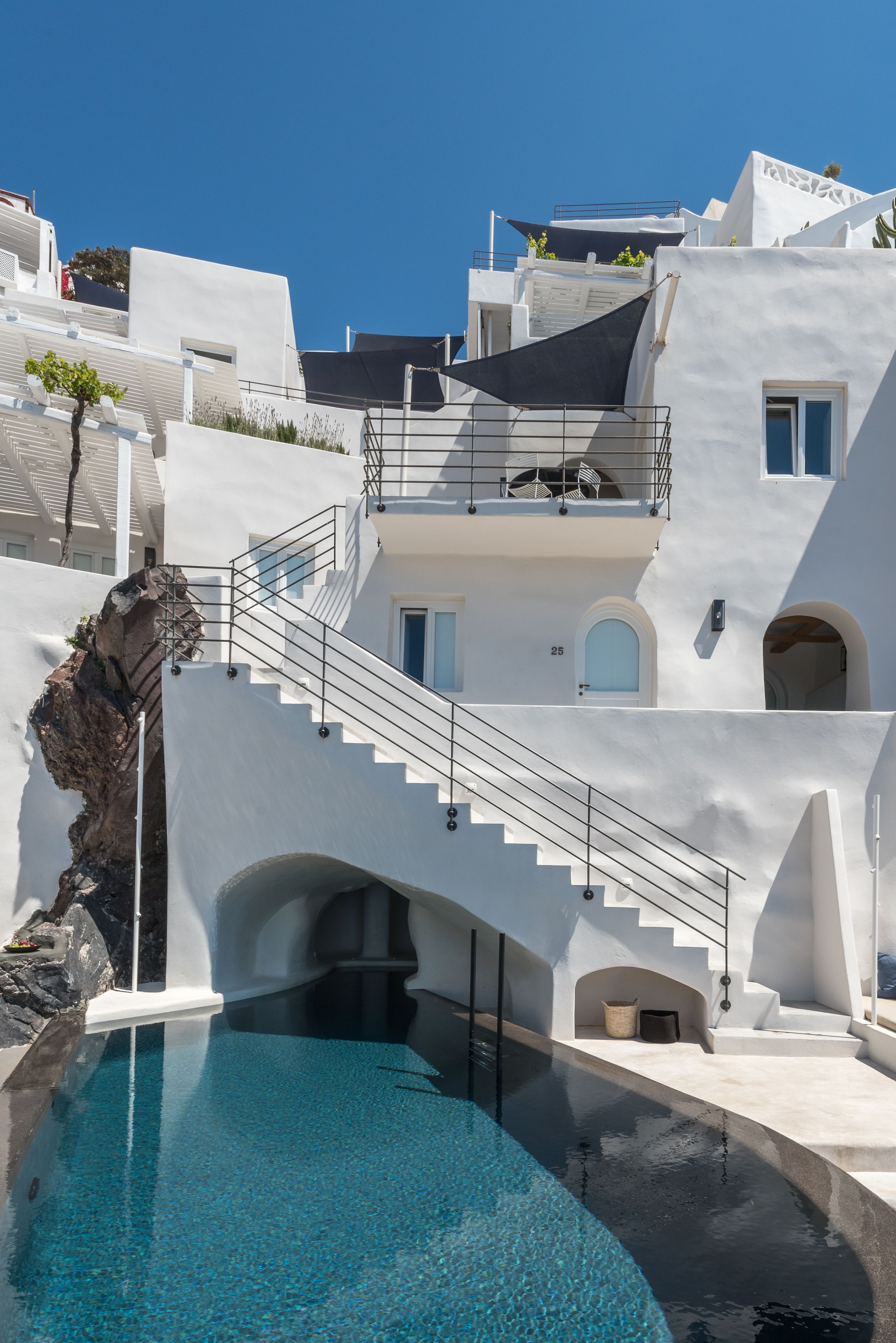 A modern building with a pool, white exterior, and a staircase leading to a balcony.