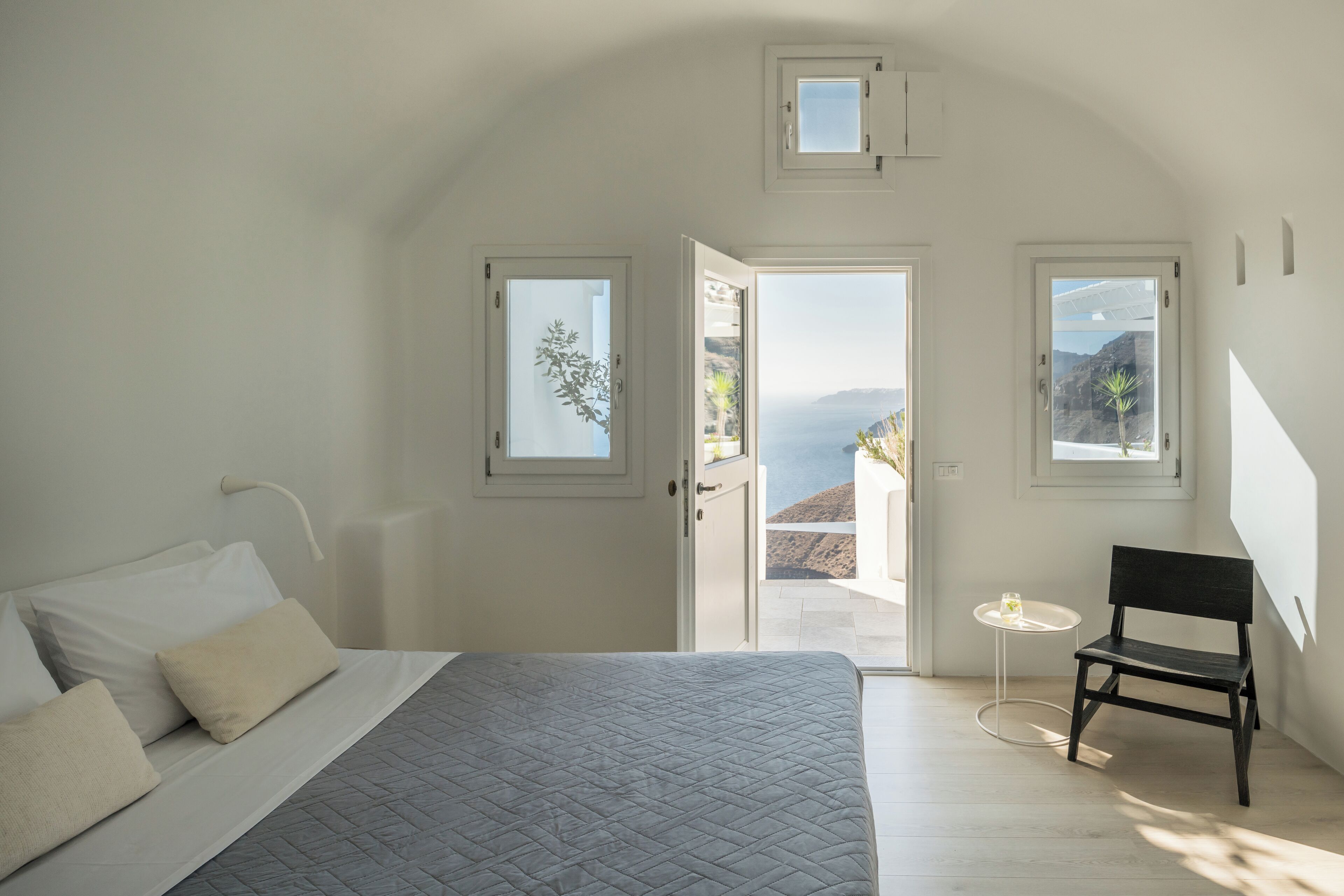 Un dormitorio con cama, una silla, una mesita y vistas al exterior.