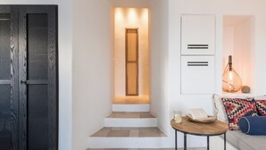 A modern interior with a wooden door, a staircase leading to a lit landing, a white cabinet, and a cozy seating area with a lamp. - Porto Fira Suites (Santorini)