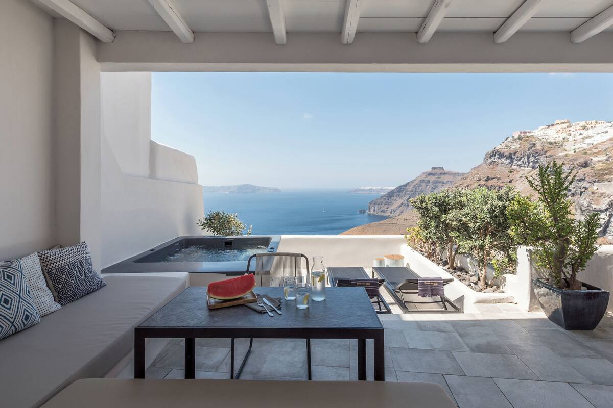 A modern outdoor seating area with a view of the sea and hills.