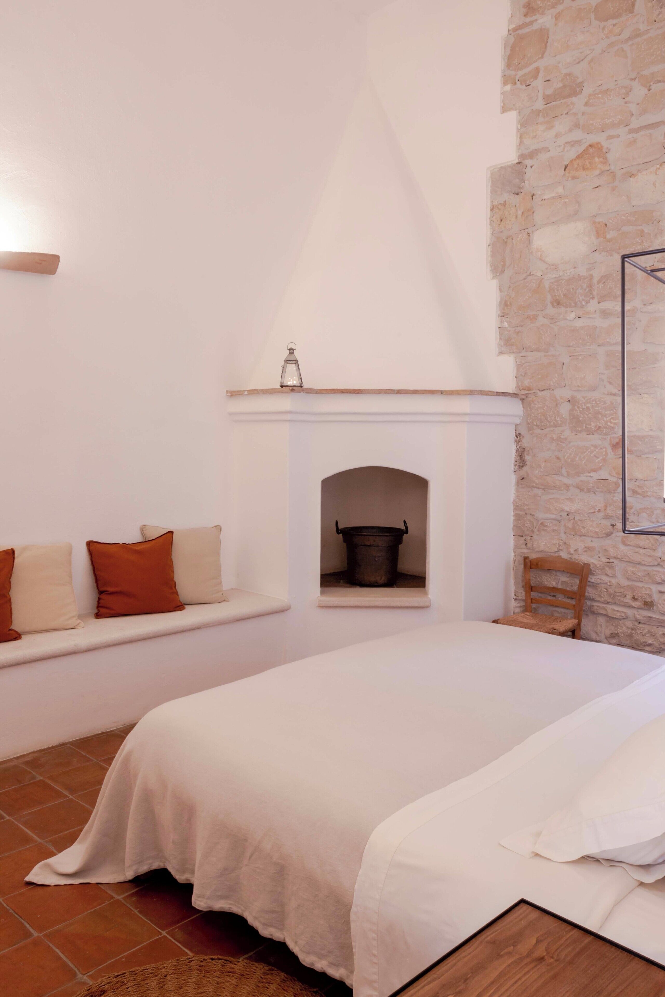 A bedroom with a stone wall, a fireplace, a bed, and a bench with cushions.