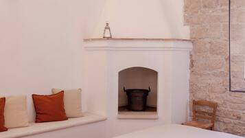 A bedroom with a stone wall, a fireplace, a bed, and a bench with cushions.