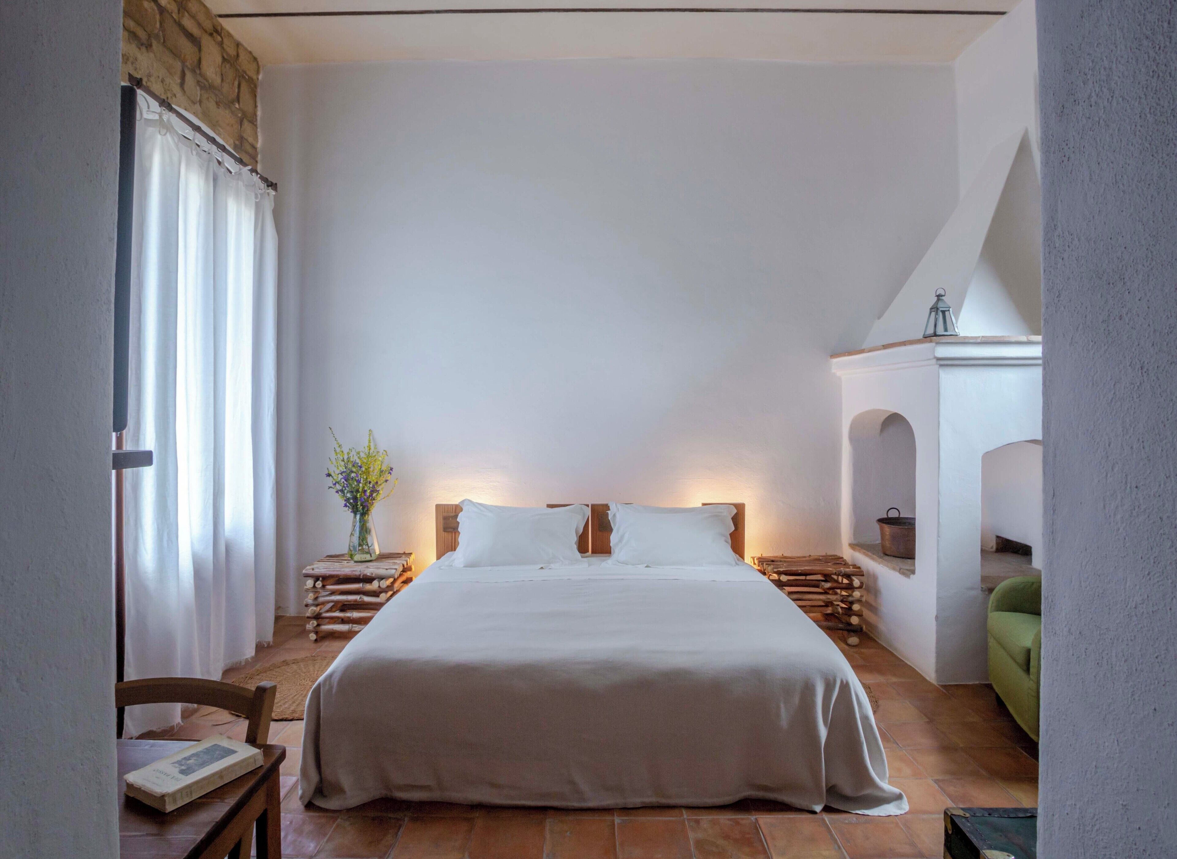 A bedroom with a large bed, wooden headboard, a nightstand with a vase of flowers, and a green chair.