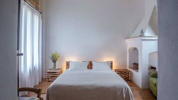 A bedroom with a large bed, wooden headboard, a nightstand with a vase of flowers, and a green chair.