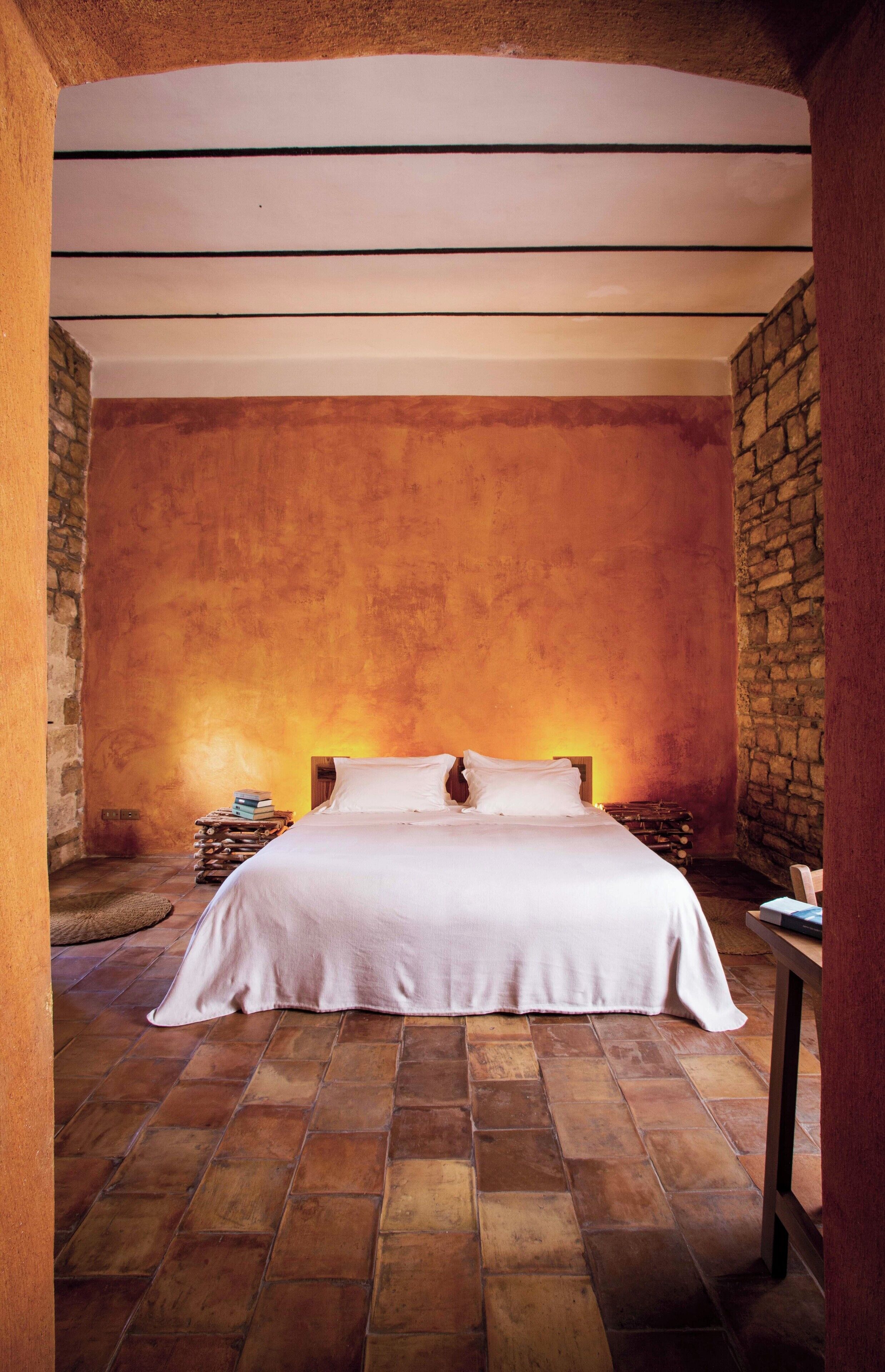 A bedroom with a large bed, stone walls, and a tiled floor.