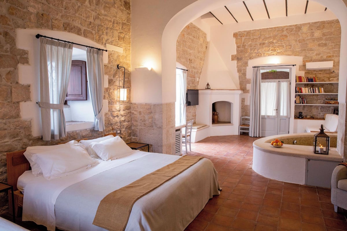 A bedroom with a large bed, a fireplace, and a stone wall.