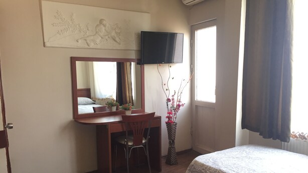 Habitación de hotel con cama, escritorio y silla, televisor, ventana con cortinas y una obra de arte en la pared.